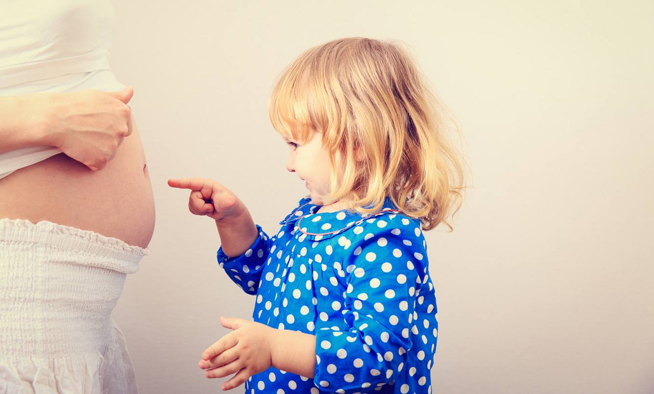 Kleines Mädchen zeigt auf den Babybauch einer Schwangeren