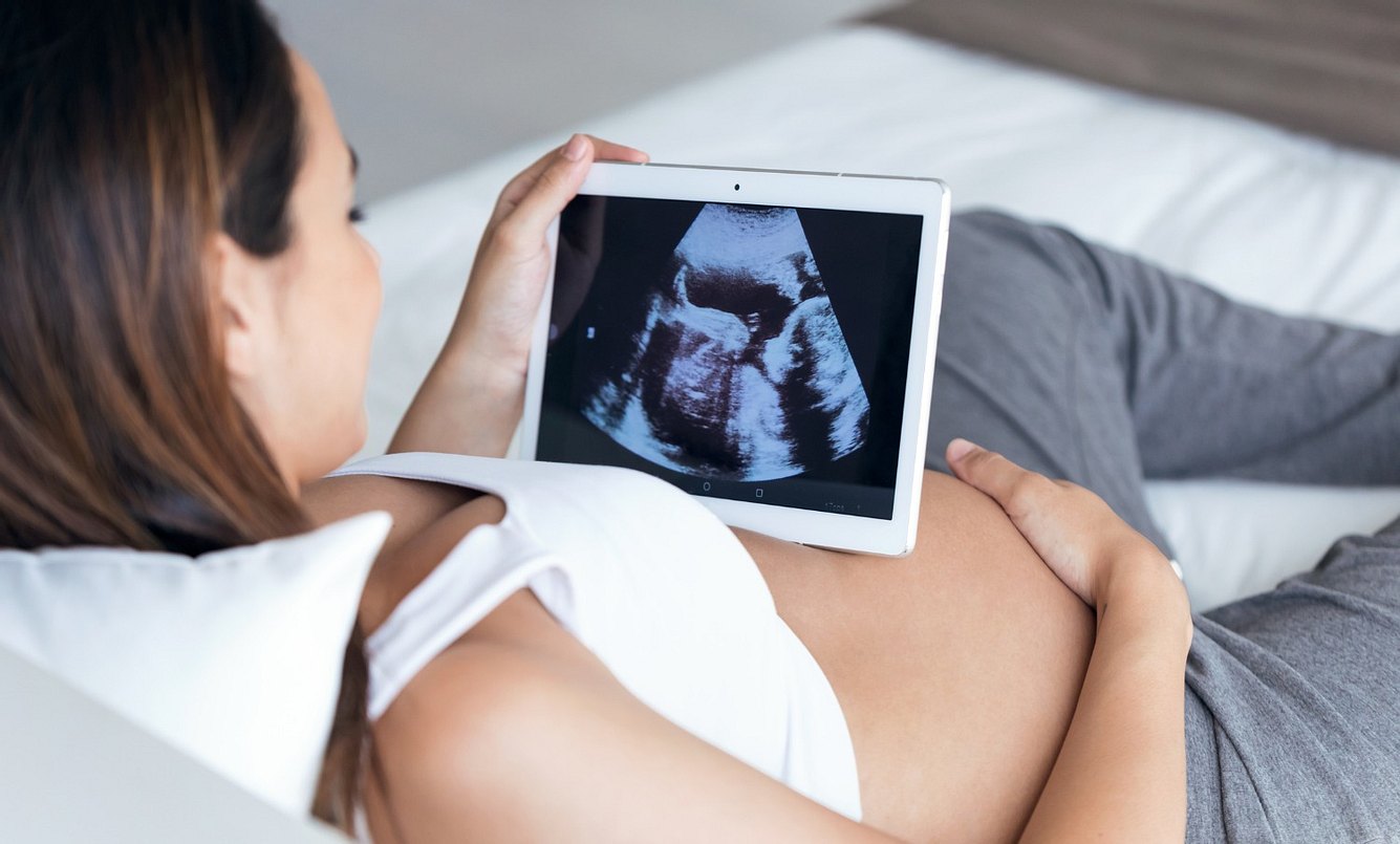 Eine schwangere Frau guckt sich ein Ultraschallbild ihres Babys auf einem Tablet an