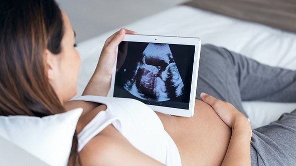 Eine schwangere Frau guckt sich ein Ultraschallbild ihres Babys auf einem Tablet an - Foto: istock_nensuria