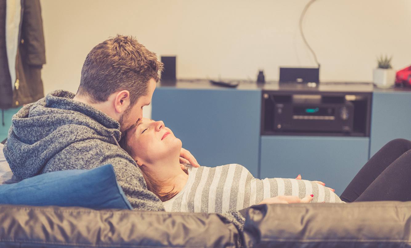 Mann und schwangere Frau liegen auf dem Sofa und genießen die Zweisamkeit