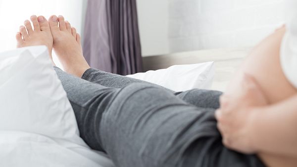 Schwangere Frau legt Beine auf eine Couch - Foto: iStock/comzeal