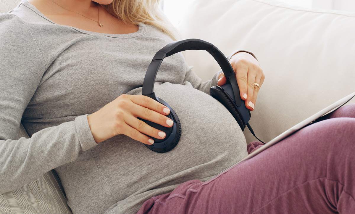 Schwangere Frau mit Kopfhörern auf dem Bauch