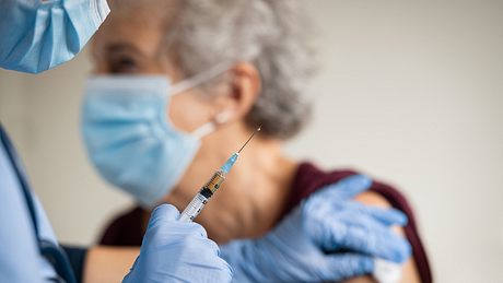 Arzt in voller Schutzkleidung gibt älterer Frau mit medizinischer Maske eine Spritze in den Oberarm - Foto: istock/Ridofranz