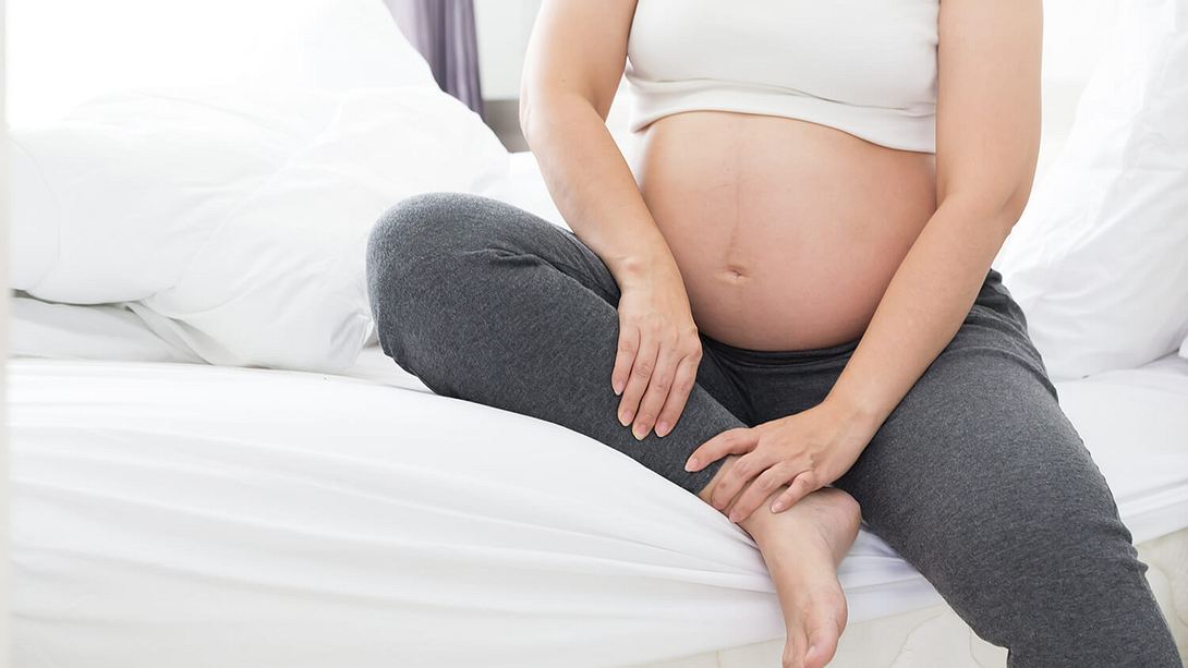 Eine schwangere Frau mit rundem Bauch sitzt auf der Bettkante - Foto: istock_comzeal