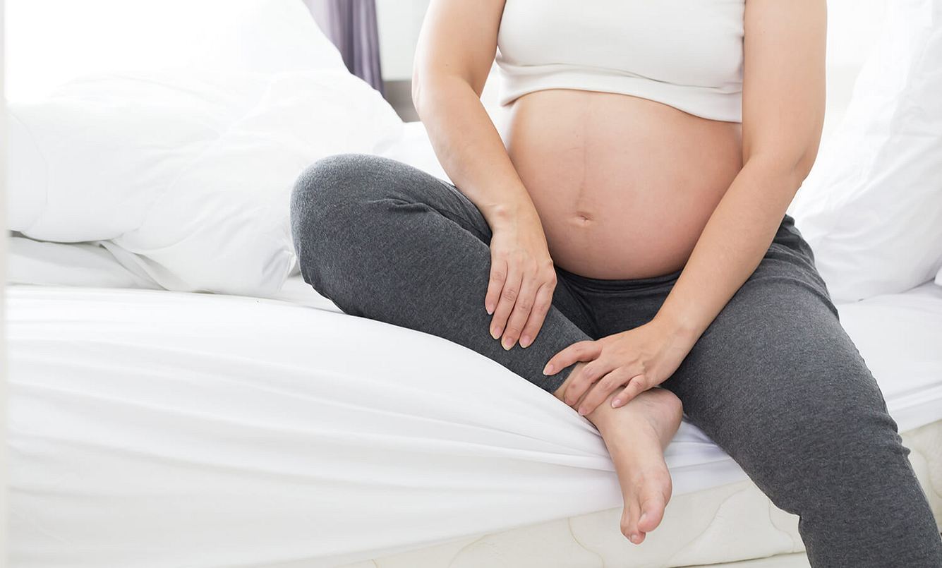 Eine schwangere Frau mit rundem Bauch sitzt auf der Bettkante
