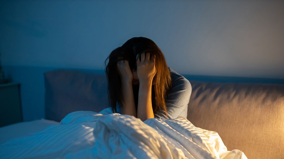 Frau wach im Bett, fässt sich an Kopf - Foto: iStock/PonyWang