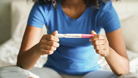 Eine Frau sitzt im Bett und hält einen Schwangerschaftstest in der Hand - Foto: iStock_diego_cervo