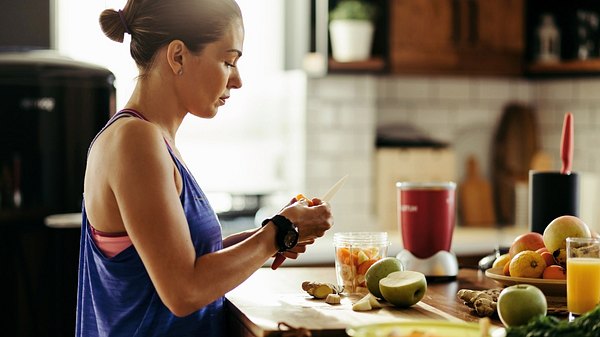 Eine Frau in Sportklamotten bereitet sich ein gesundes Frühstück zu - Foto: istock_Drazen Zigic
