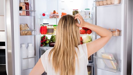 Frau steht fragend vor vollem Kühlschrank - Foto: istock/andreypopov
