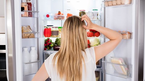 Frau steht fragend vor vollem Kühlschrank - Foto: istock/andreypopov