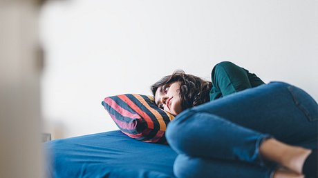 Junge Frau mit ADHS und Depression liegt traurig auf einem Bett - Foto: iStock/recep-bg