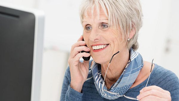 Eine ältere Frau telefoniert vor einem Computer - Foto: Fotolia