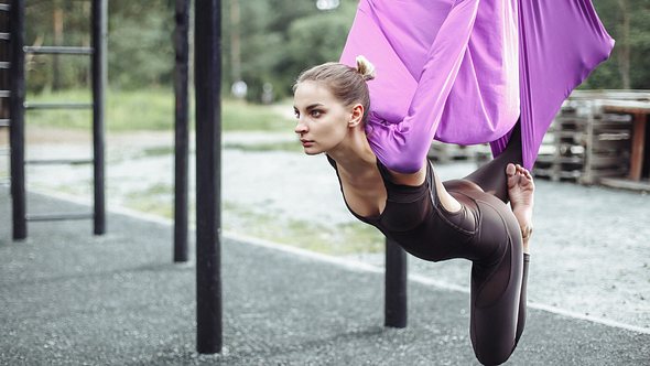 Frau macht Aerial Yoga mit lila Tuch - Foto: iStock/Artem Ermilov