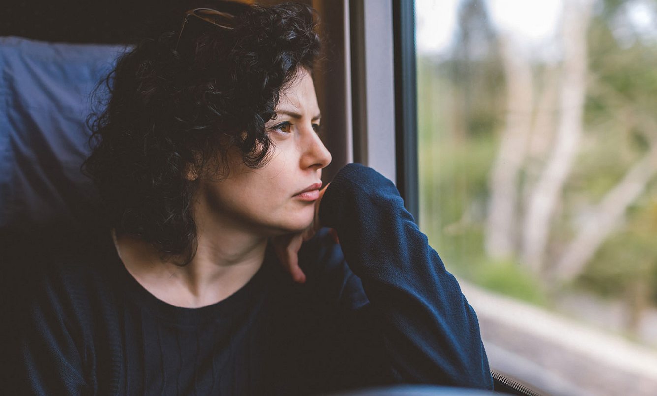 Eine Frau sitzt im Zug und schaut aus dem Fenster