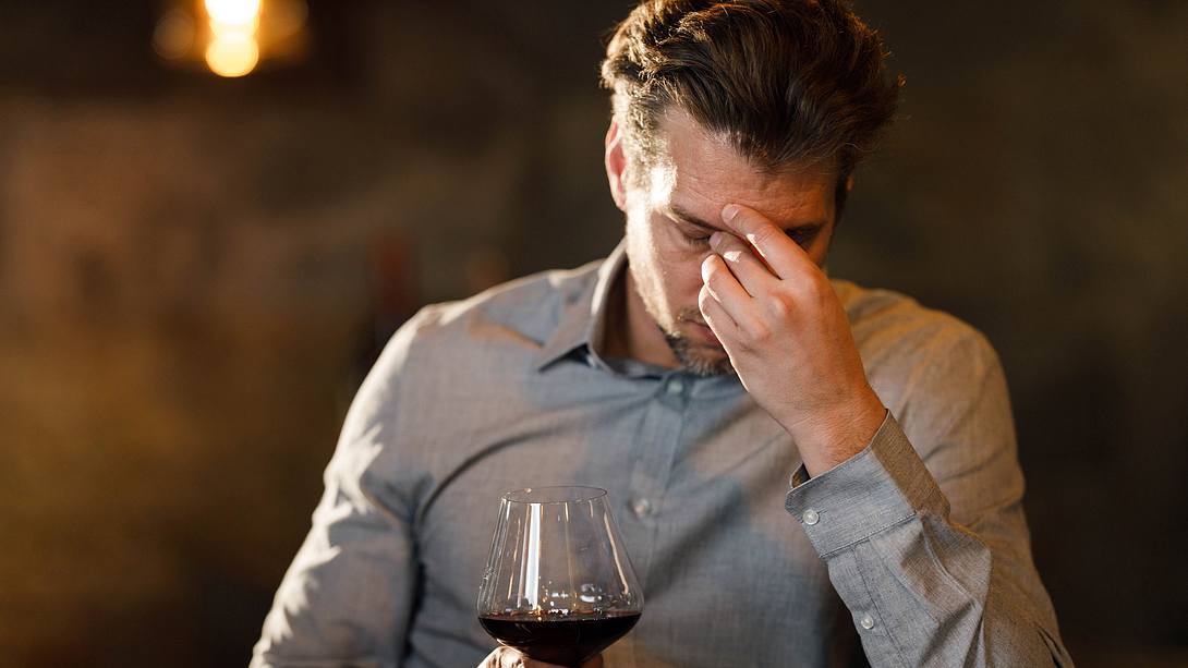 Mann mit Rotweinglas fasst sich müde an den Kopf - Foto: iStock/skynesher