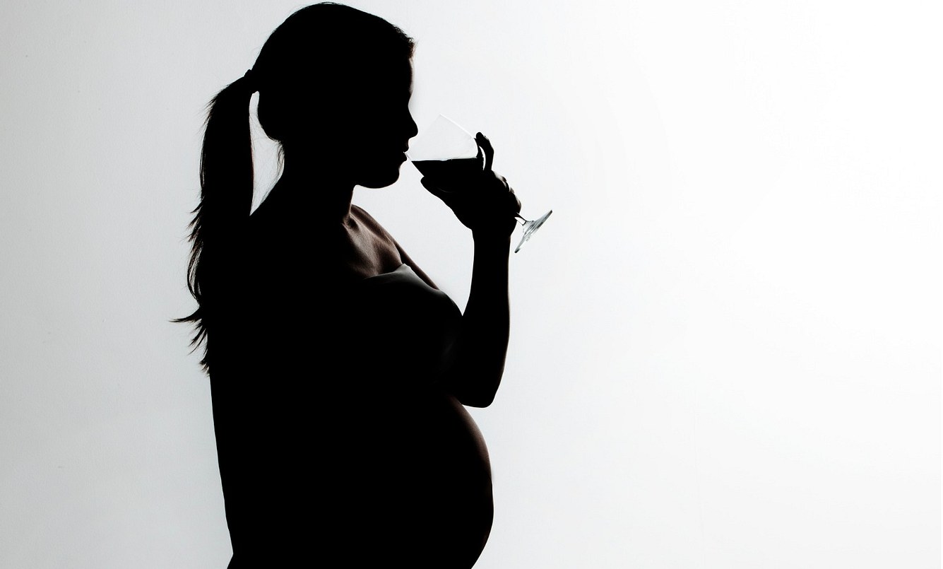 Eine schwangere Frau trinkt aus einem Weinglas