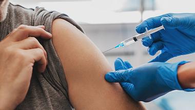 Mann erhält eine Impfung – Ärztin mit Schutzhandschuhen setzt Spritze in den Oberarm - Foto: iStock/Inside Creative House