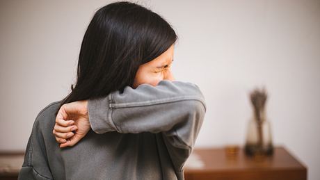Eine Frau niest in ihre Armbeuge - Foto: iStock/agrobacter