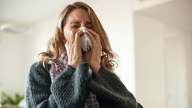 Eine Frau niest zuhause - Foto: iStock/Mindful Media