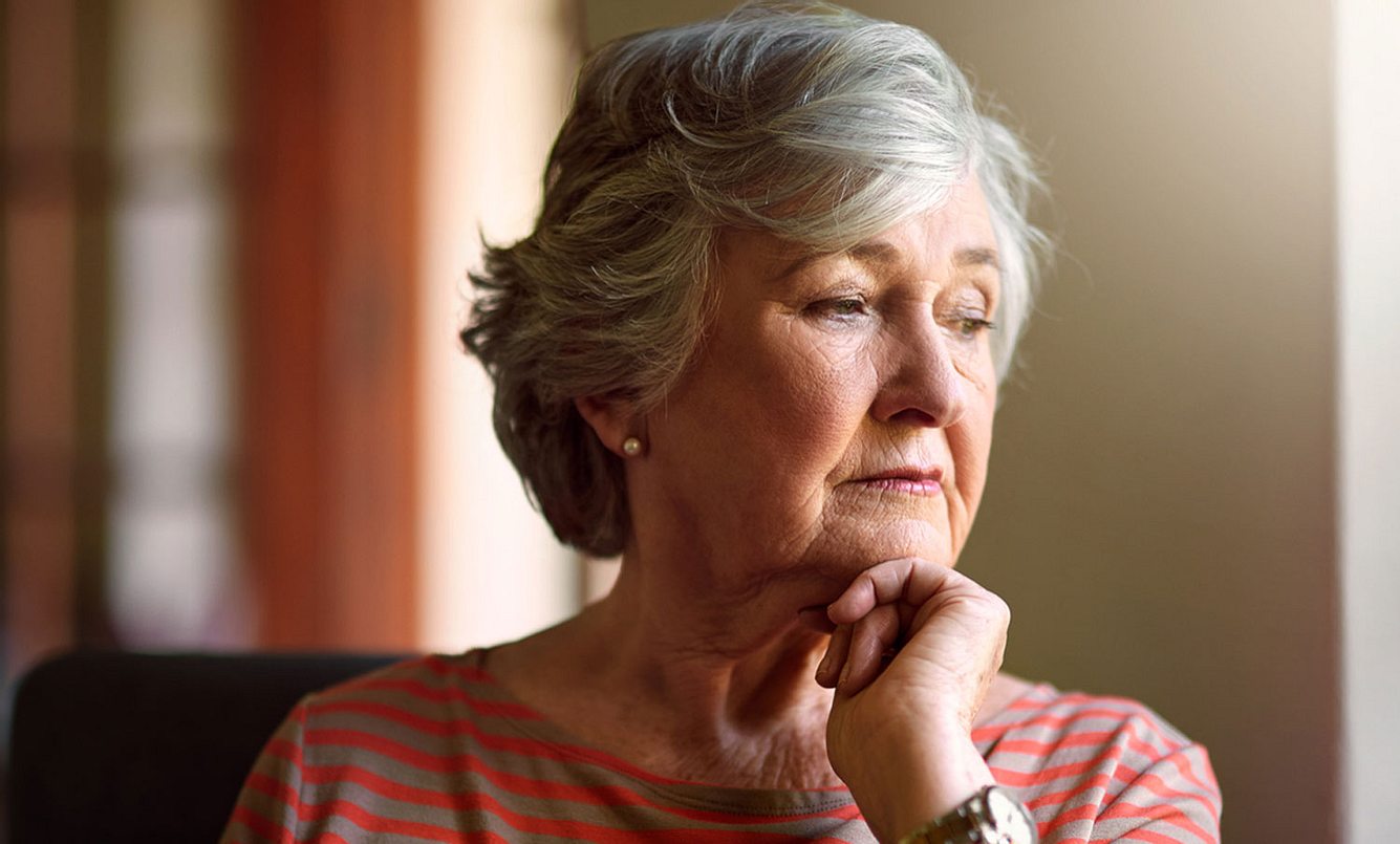 Ältere Dame schaut müde und traurig aus dem Fenster