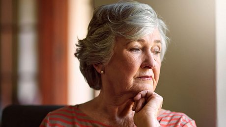 Ältere Dame schaut müde und traurig aus dem Fenster - Foto: iStock/PeopleImages