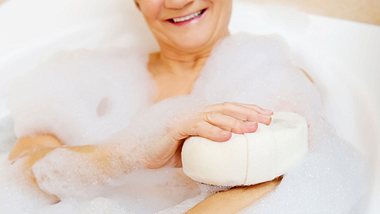 Ältere Dame sitzt lächelnd in der Badewanne und schäumt sich mit einem Schwamm ein - Foto: iStock/Piotr Marcinski