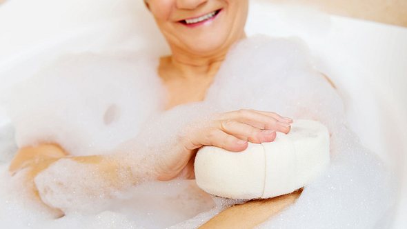 Ältere Dame sitzt lächelnd in der Badewanne und schäumt sich mit einem Schwamm ein - Foto: iStock/Piotr Marcinski