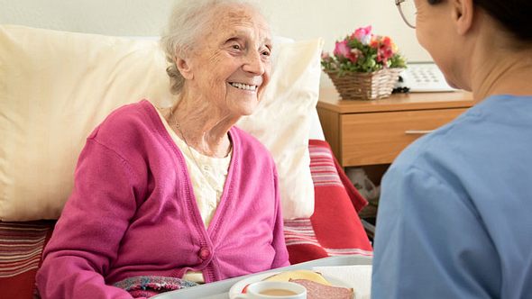 Pflegerin reicht Seniorin im Bett Essen - Foto: iStock/FredFroese