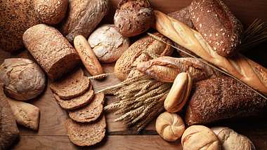Eine Auswahl verschiedener Brote und Ähren auf einem Holzuntergrund - Foto: istock/Floortje