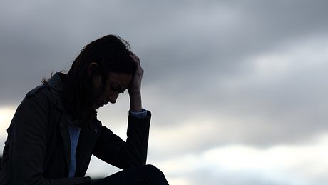 Eine traurig wirkende Frau stützt den Kopf auf ihre Hand - Foto: iStock-AntonioGuillem