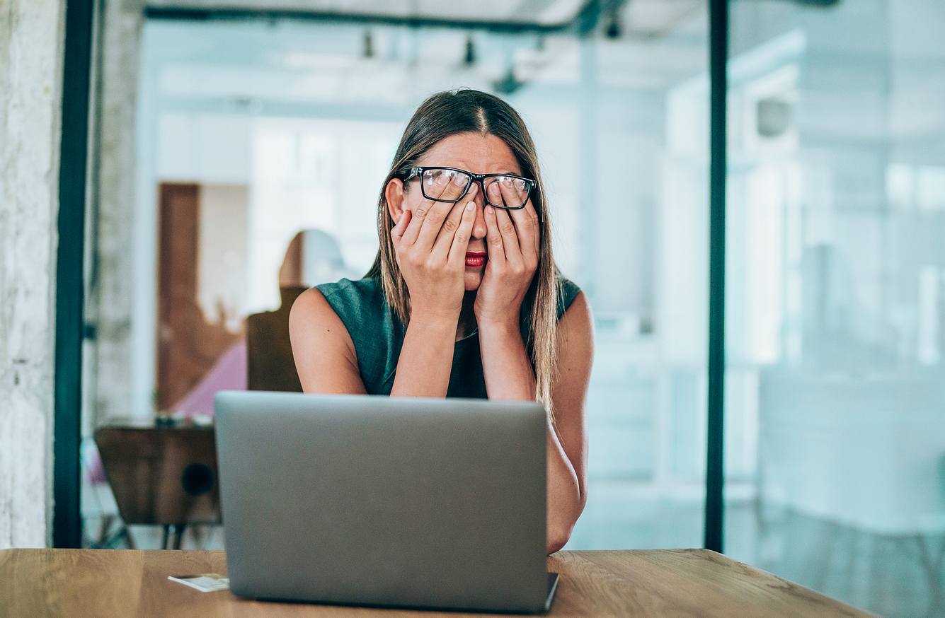 Eine Frau sitzt am Schreibtisch und reibt sich verzweifelt die Augen aus Angst vor der Arbeit