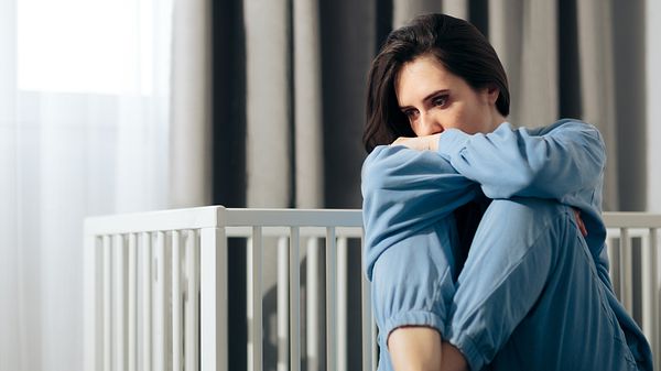 Frau sitzt traurig vor Babybett - Foto: iStock/nicoletaionescu