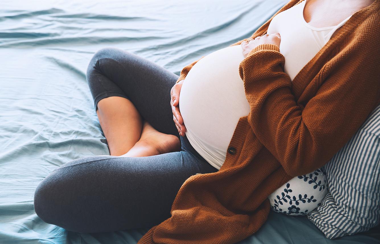 angst-vor-schwangerschaft Frau sitzt auf dem Bett und hält sich den Bauch.