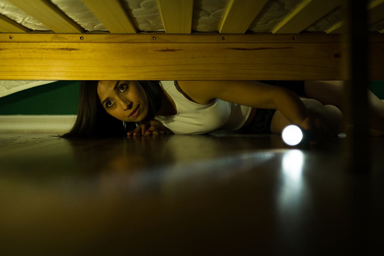 arachnophobie Frau mit Arachnophobie schaut mit einer Taschenlampe unter das Bett
