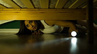 Frau mit Arachnophobie schaut mit einer Taschenlampe unter das Bett - Foto: iStock/Antonio_Diaz