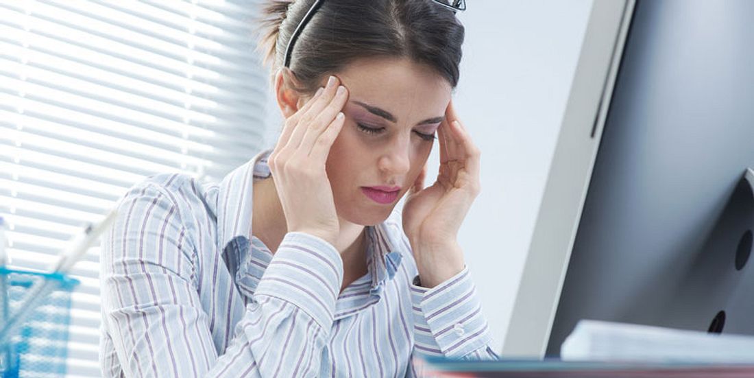 Frau mit Kopfschmerzen vor Computer