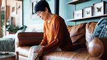 Eine Frau sitzt auf einer Couch und hält sich ihr schmerzendes Knie fest. - Foto: iStock / AsiaVision