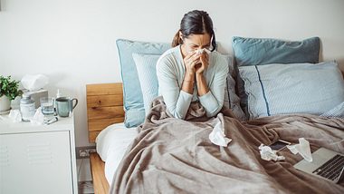 Eine Frau sitzt im Bett und putzt sich die Nase - Foto: iStock/﻿svetikd