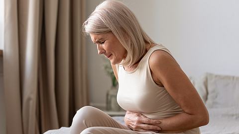 Eine Frau hält sich mit beiden Händen ihren aufgeblähten Bauch  - Foto: iStock_fizkes