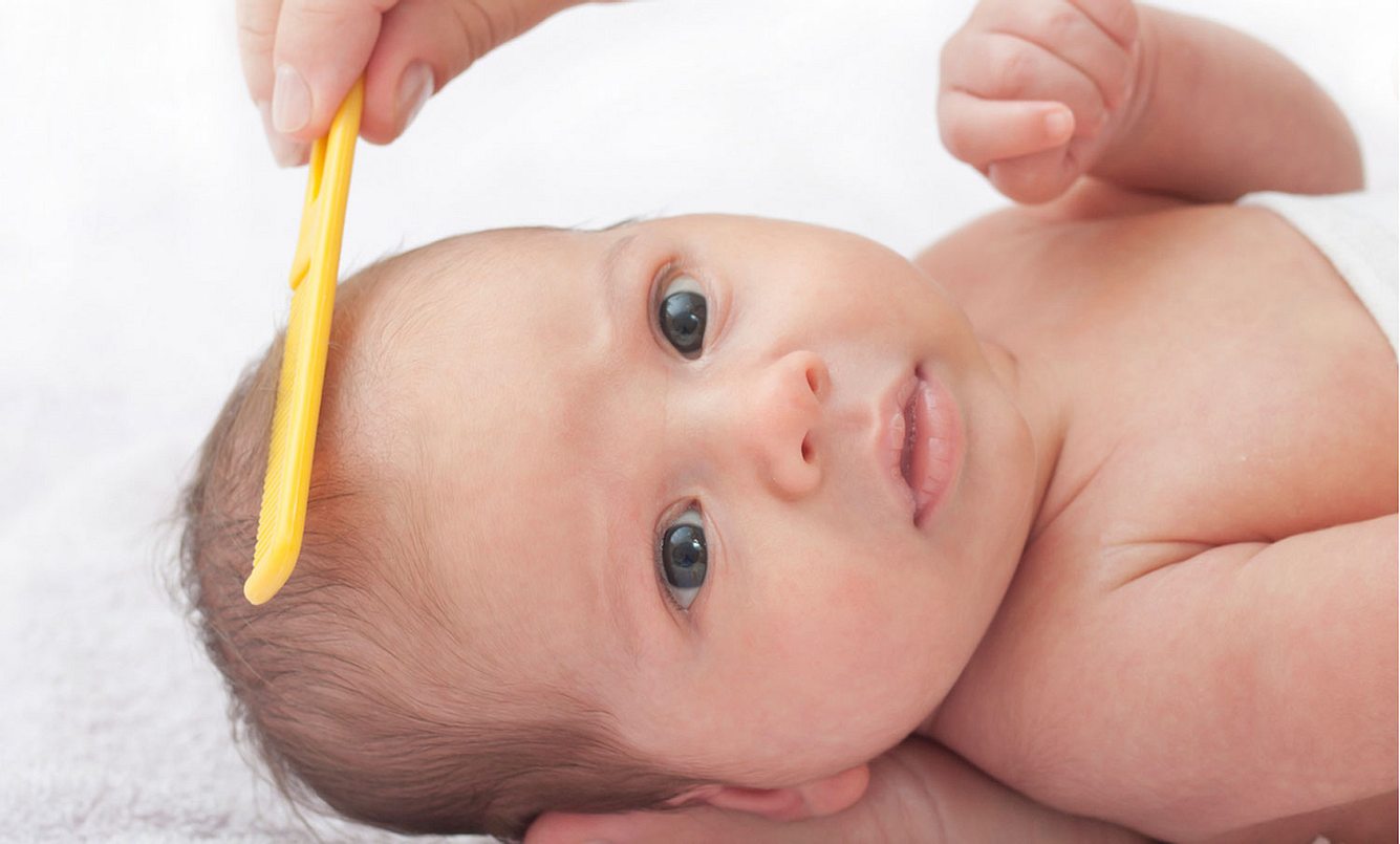 Mutter entfernt Milchschorf bei einem Baby mit dem Kamm
