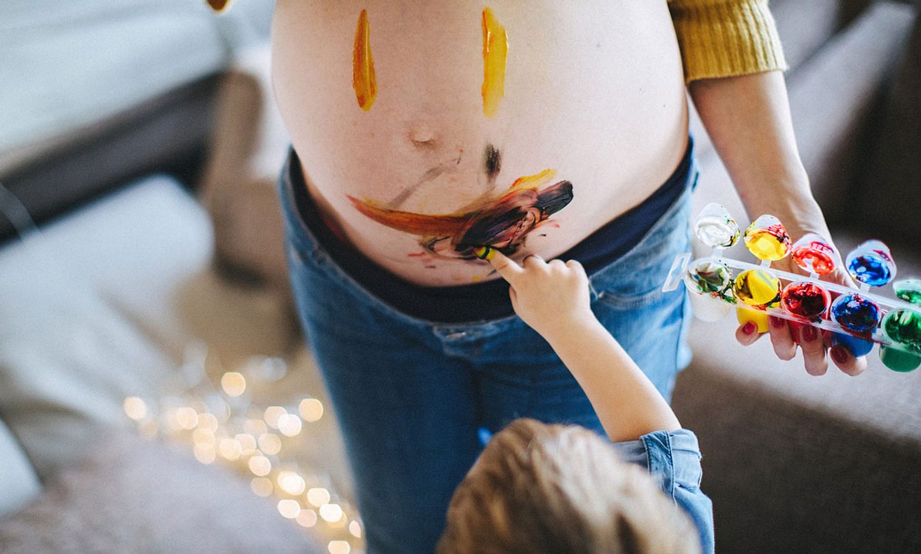 Kleinkind bemalt den Bauch seiner schwangeren Mutter