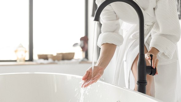 Eine Frau in Bademantel prüft die Temperatur des Badewassers - Foto: istock_bymuratdeniz