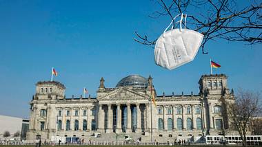 Reichstag in Berlin, im Vordergrund hängt eine FFP2-Maske an einem Baum - Foto: IMAGO/Steinach