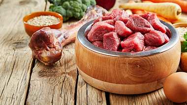 Holzschlüssel mit roh geschnittenem Fleisch steht auf einem Holztisch mit anderen Lebensmitteln im Hintergrund - Foto: iStock/imagoimages/Panthermedia