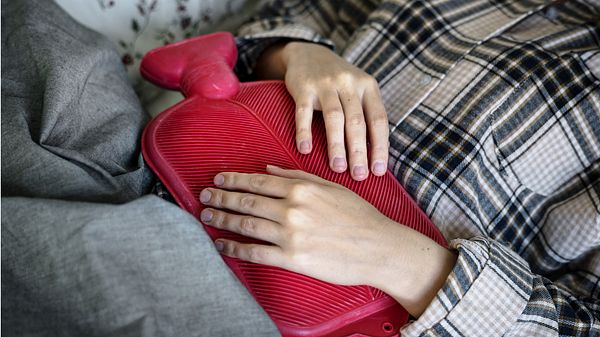 Eine Frau liegt im Bett mit einer Wärmflasche auf dem Bauch - Foto: iStock/Rawpixel