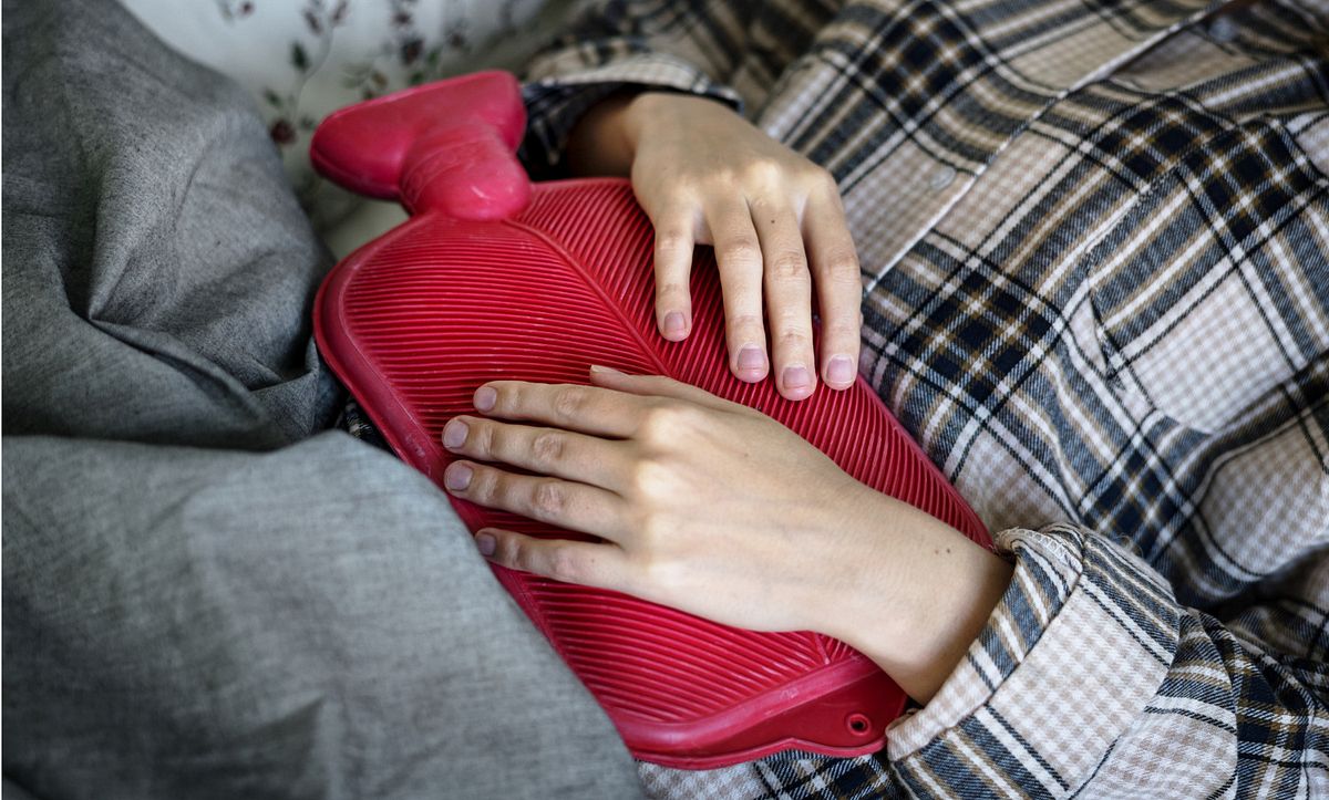Eine Frau liegt im Bett mit einer Wärmflasche auf dem Bauch