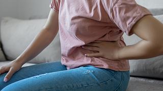 Eine Frau sitzt mit Bauchschmerzen auf dem Sofa - Foto: iStock_bymuratdeniz