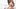 Frau sitzt auf dem Bett und hält sich Wärmflasche auf den Bauch - Foto: iStock/PeopleImages