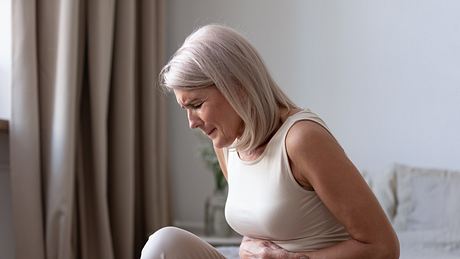 Frau mit Bauchschmerzen in der Mitte hält sich den Bauch - Foto: iStock/fizkes