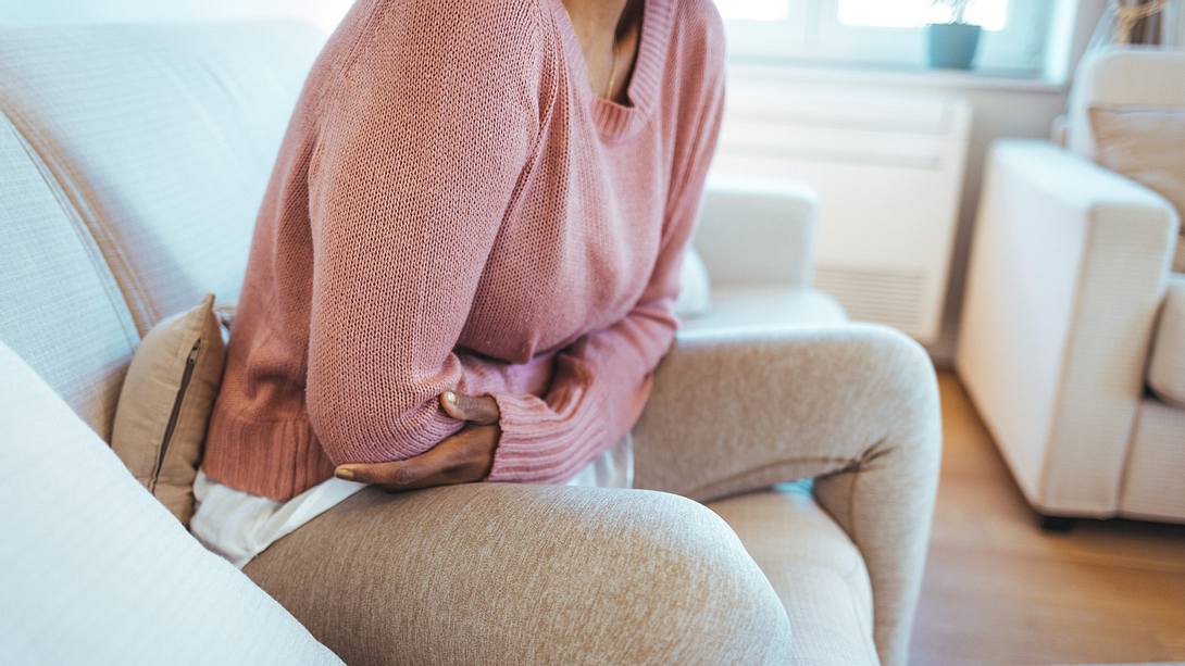 Eine Frau sitzt mit Bauchschmerzen auf dem Sofa - Foto: istock_dragana991